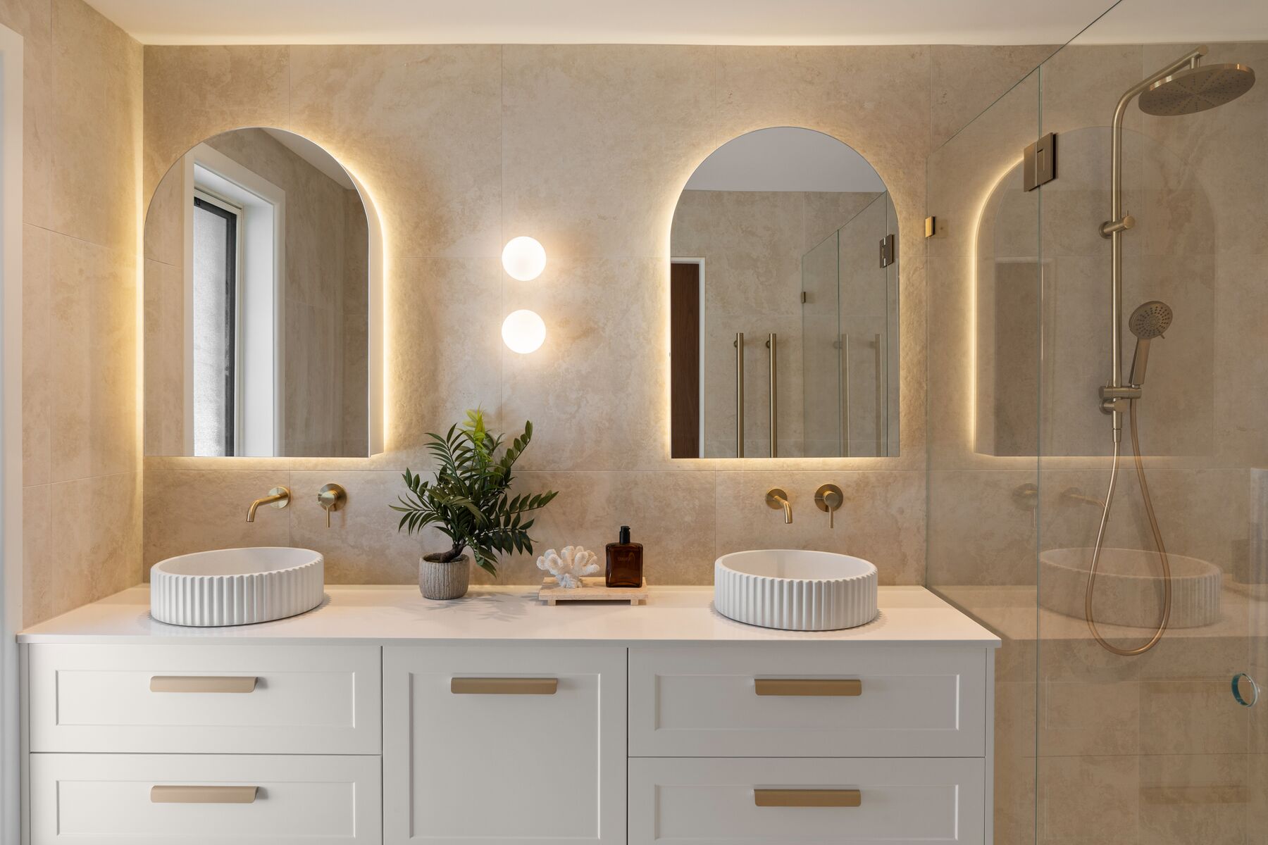 Bathroom with a double vanity, backlit arched mirrors and wall lights