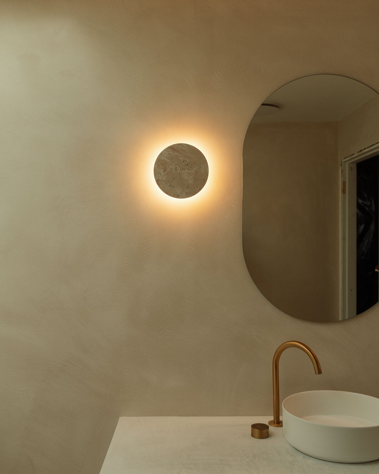 Bathroom vanity with a round wall light, oval mirror and brass tapware