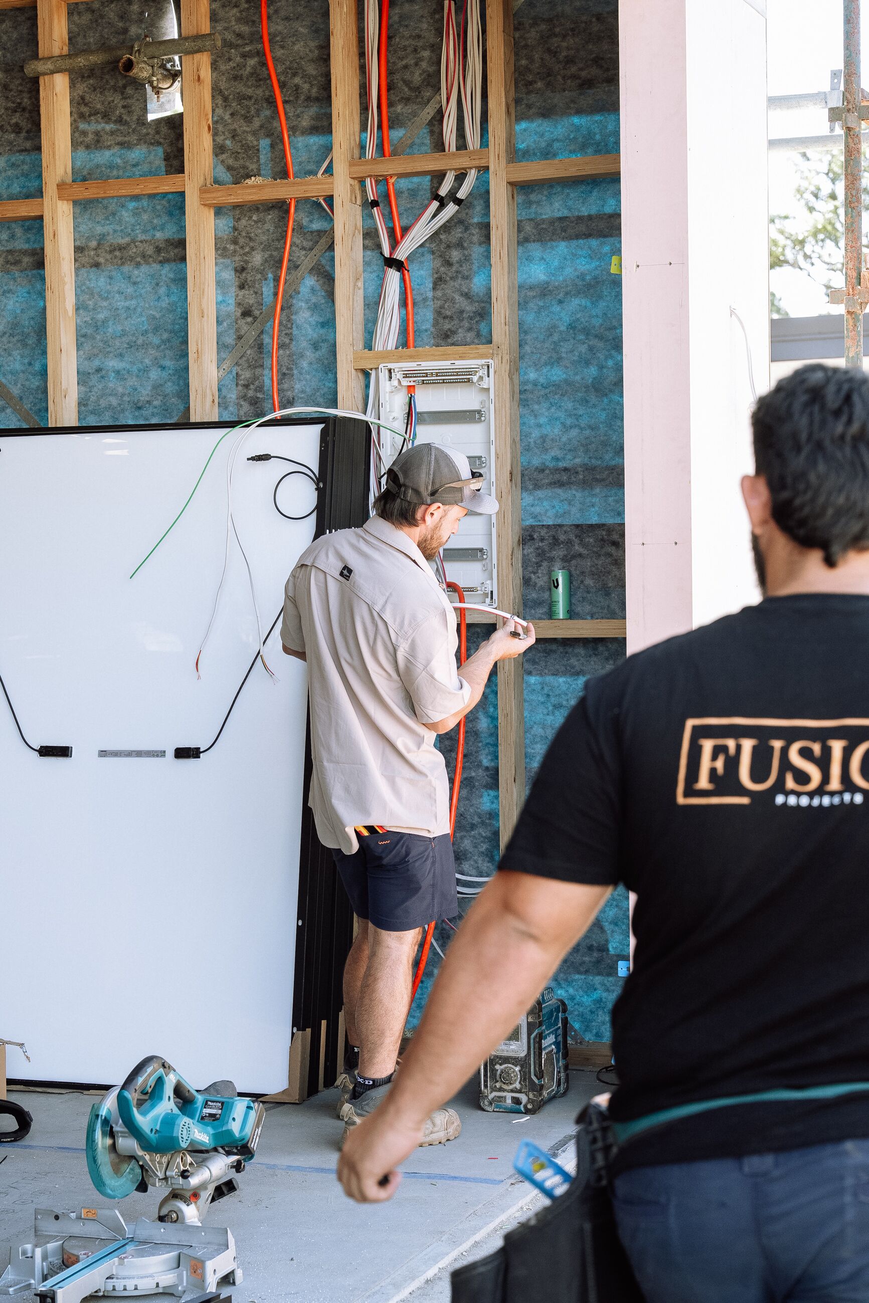Fusion electricians installing a home battery on a wall inside a timber frame