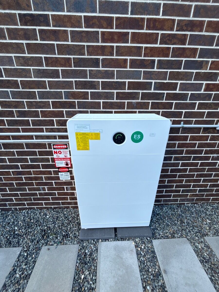 Fusion electricians installing a home battery on a wall inside a timber frame