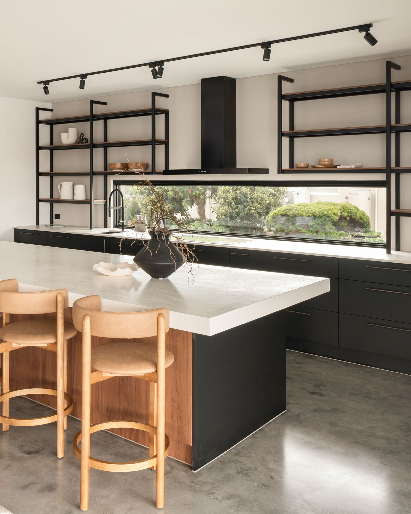 Black kitchen with track lighting, open shelving and a long stone bench