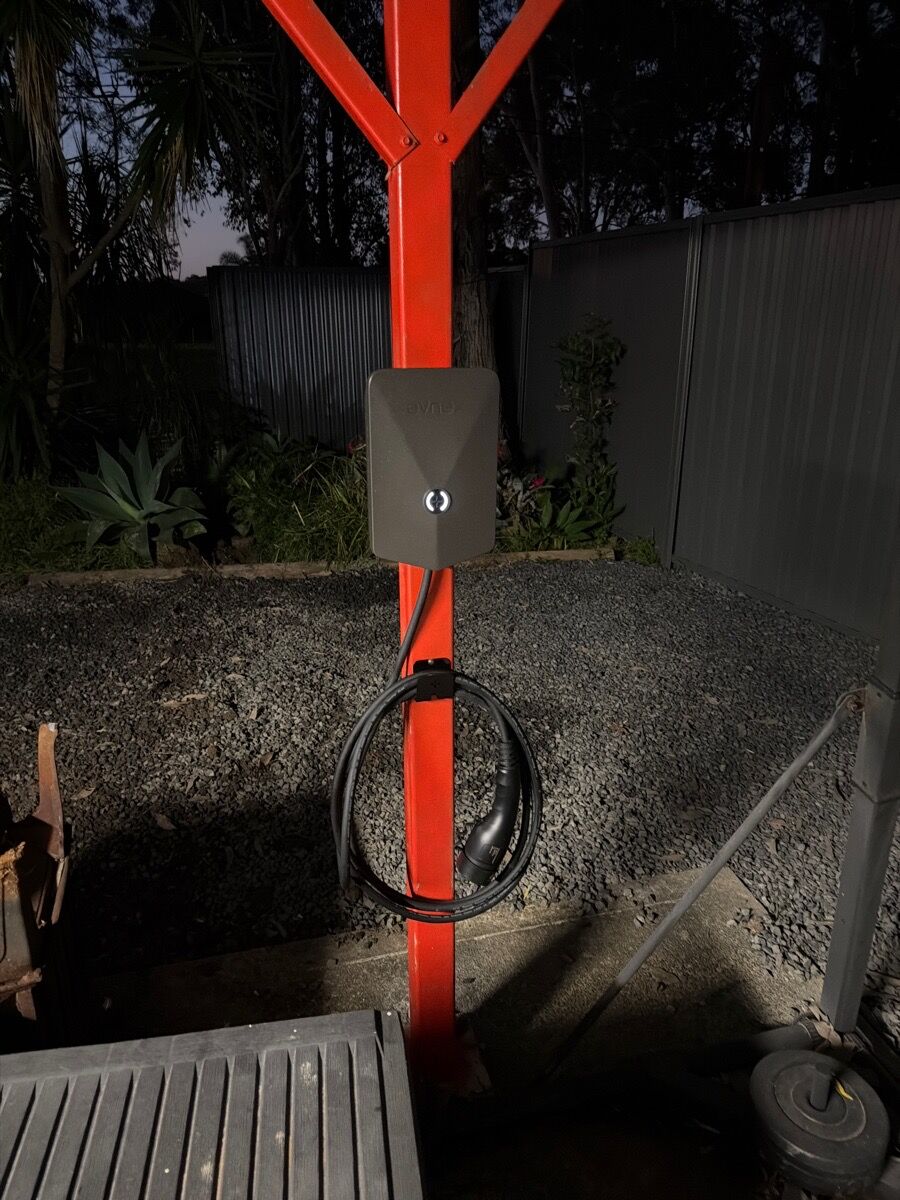 Wall-mounted home EV charger with its cable coiled on a painted brick wall
