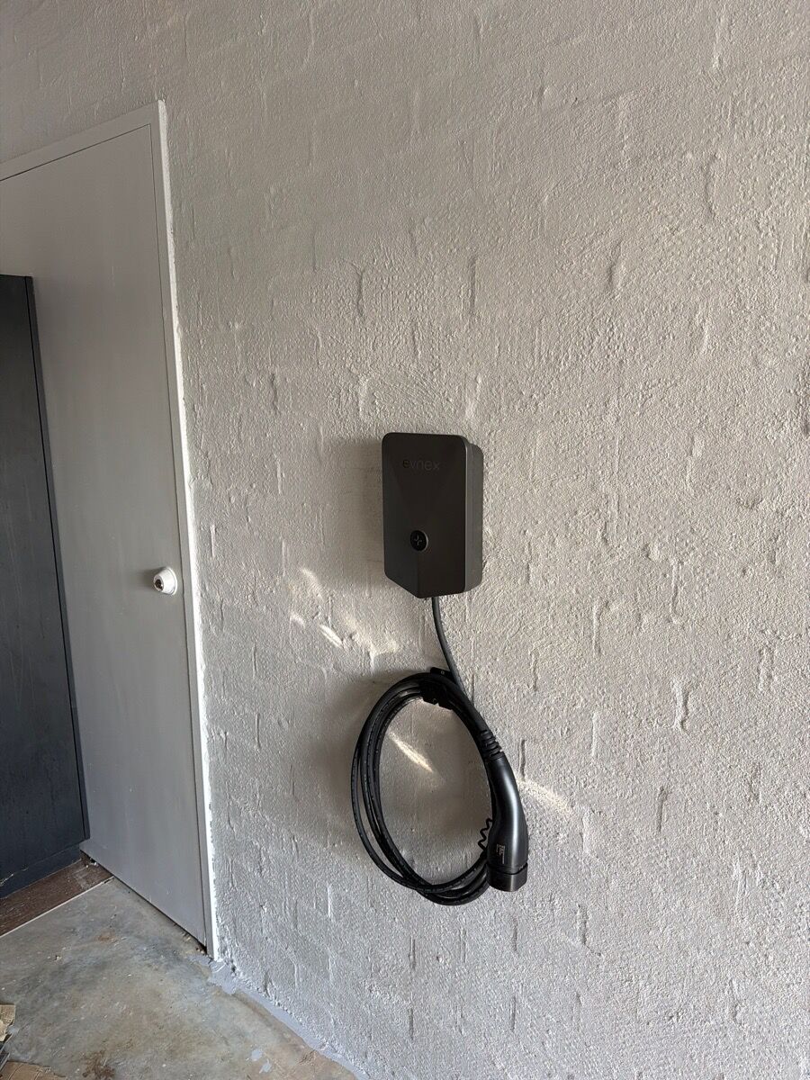Wall-mounted home EV charger with its cable coiled on a painted brick wall
