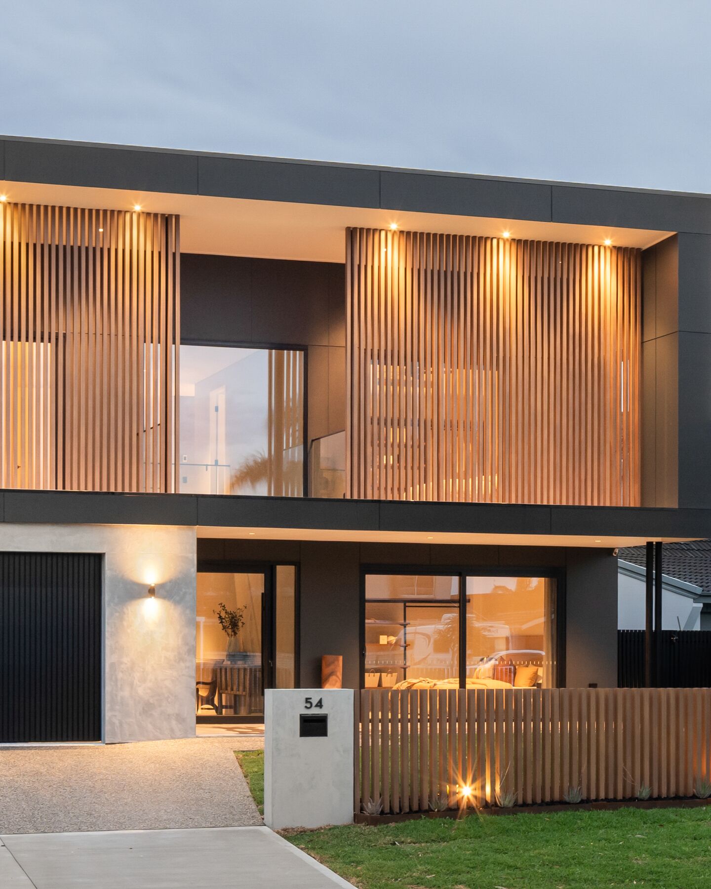 Two-storey modern home at dusk with timber battens and exterior lighting