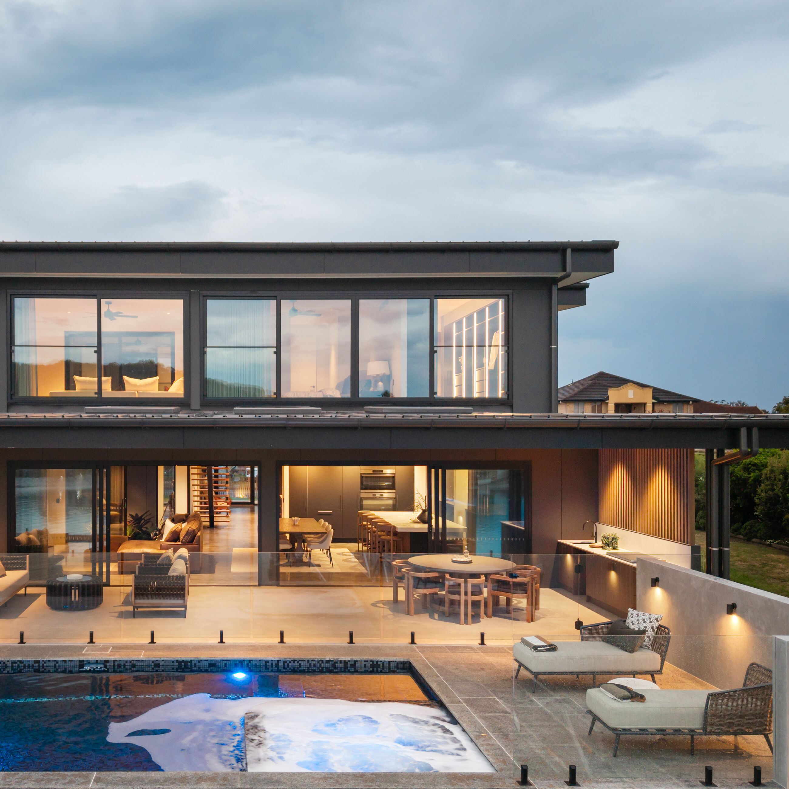 Drone view of a lit pool and alfresco at a modern home at dusk
