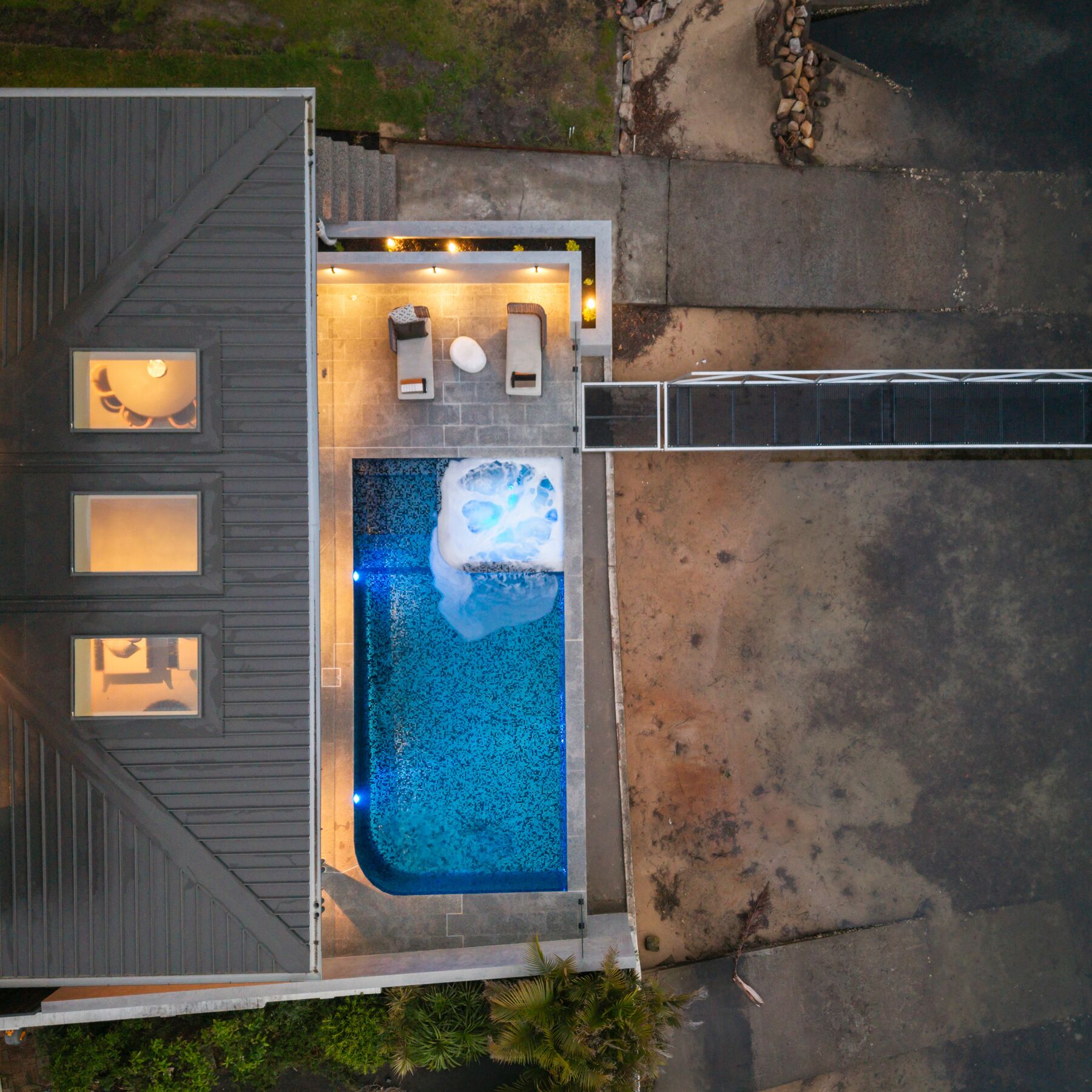 Drone view of a lit pool and alfresco at a modern home at dusk