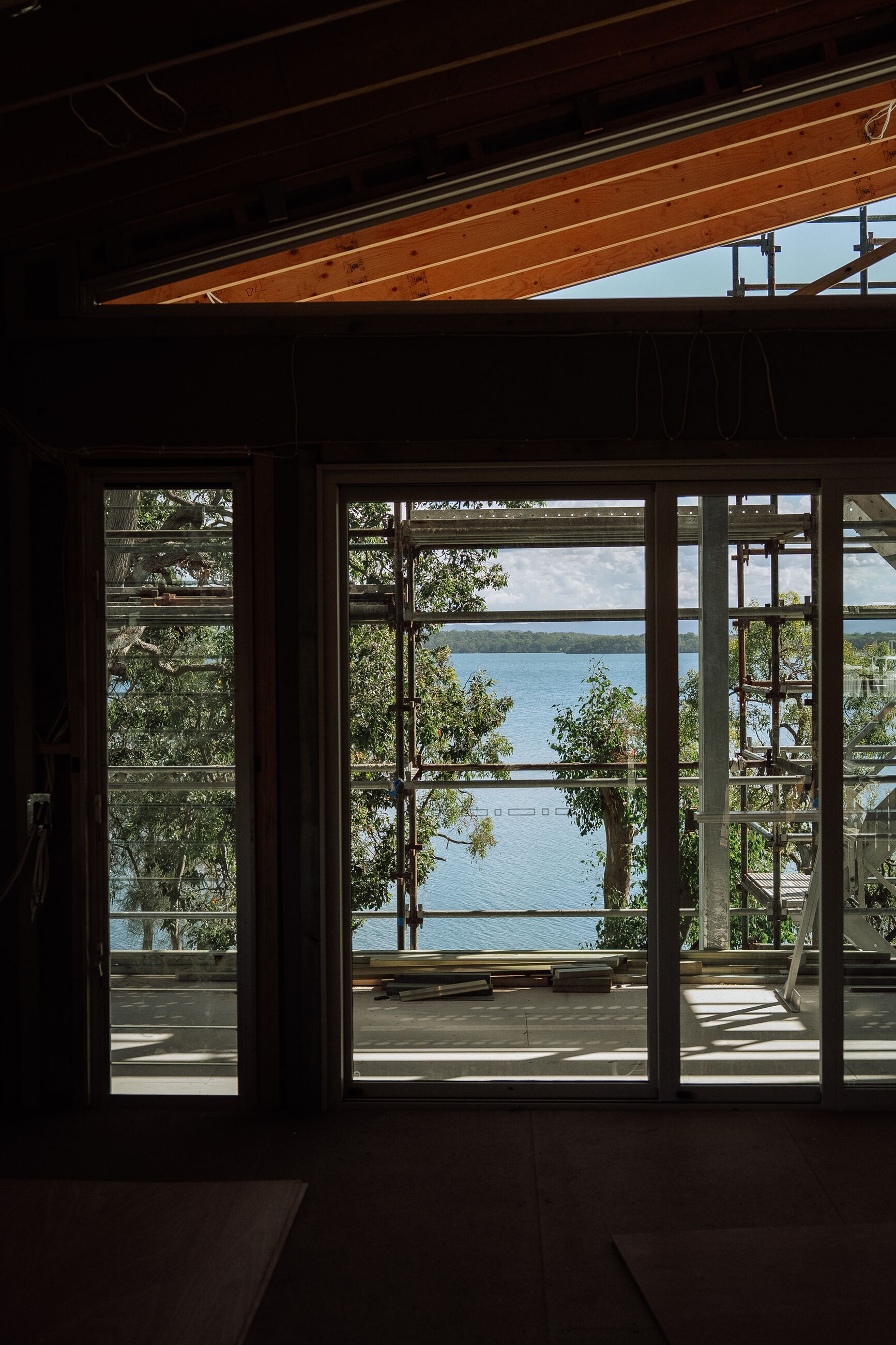 House under renovation with exposed raked roof framing and scaffolding, water views beyond