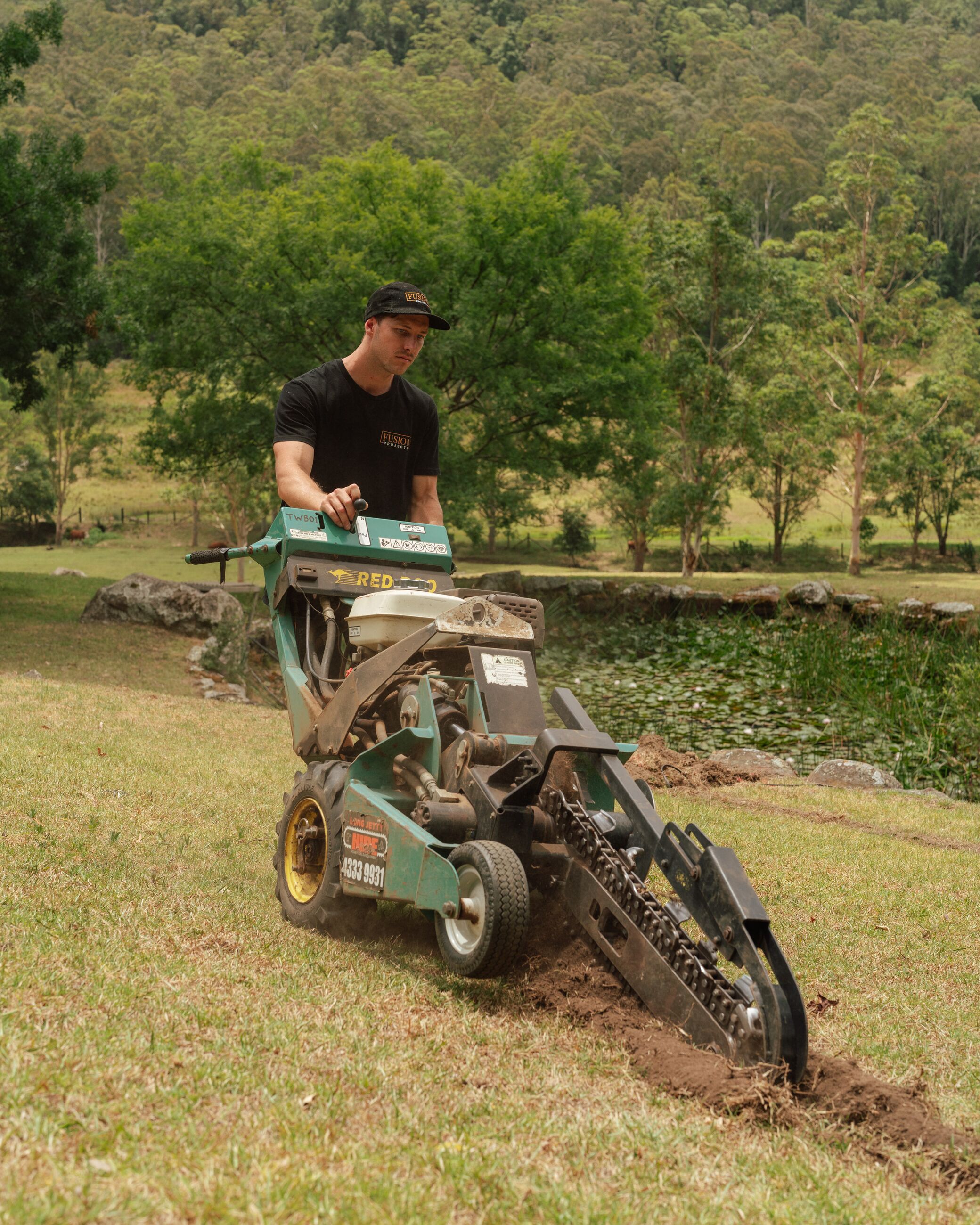Fusion crew member cutting a cable trench across a lawn with a trencher